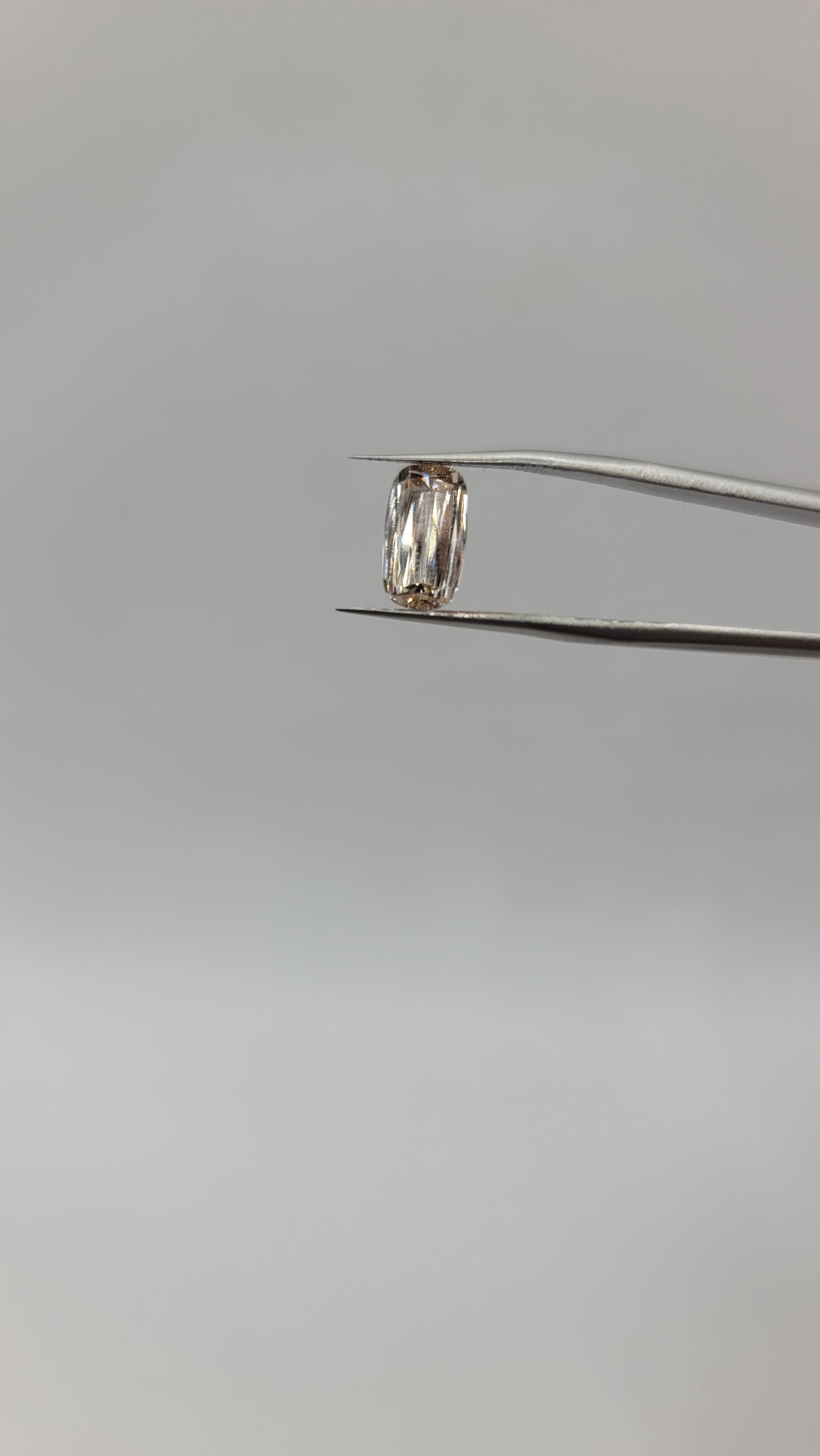 A lab grown crisscut diamond held by metal tweezers against a plain light gray background.