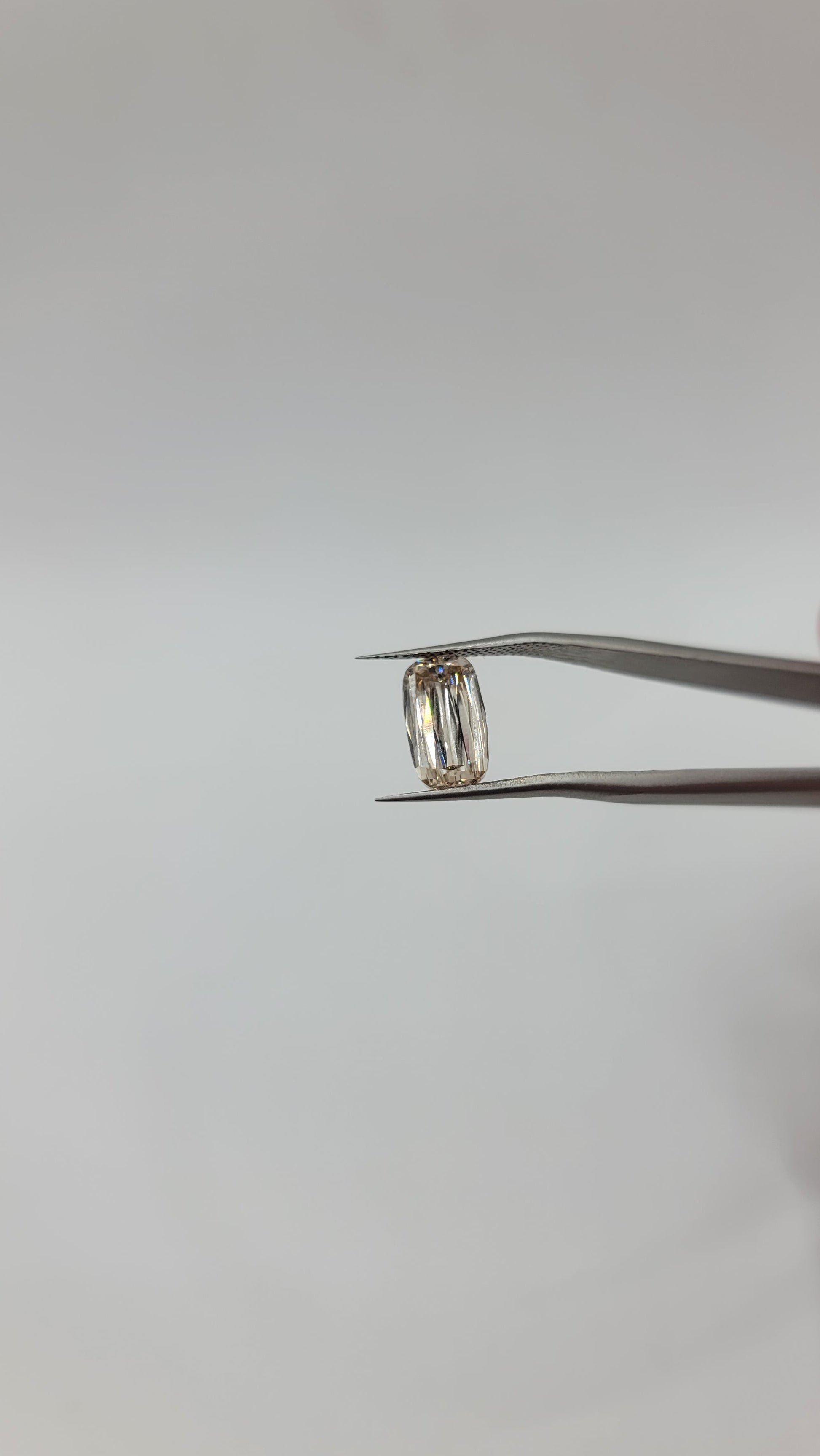 A lab grown crisscut diamond held between metal tweezers against a plain light gray background.