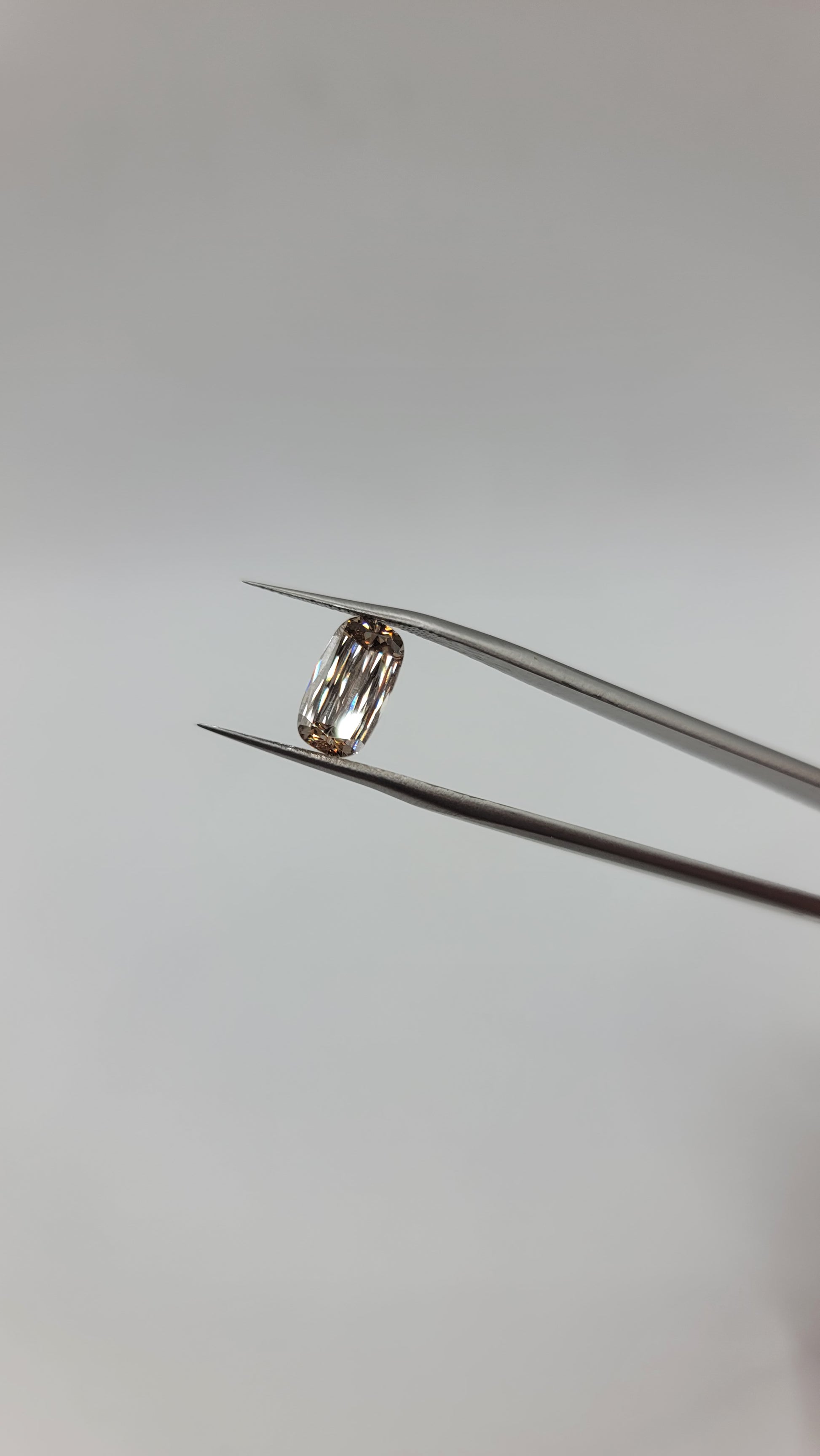 A lab grown crisscut diamond held between a pair of fine metal tweezers against a plain light gray background.