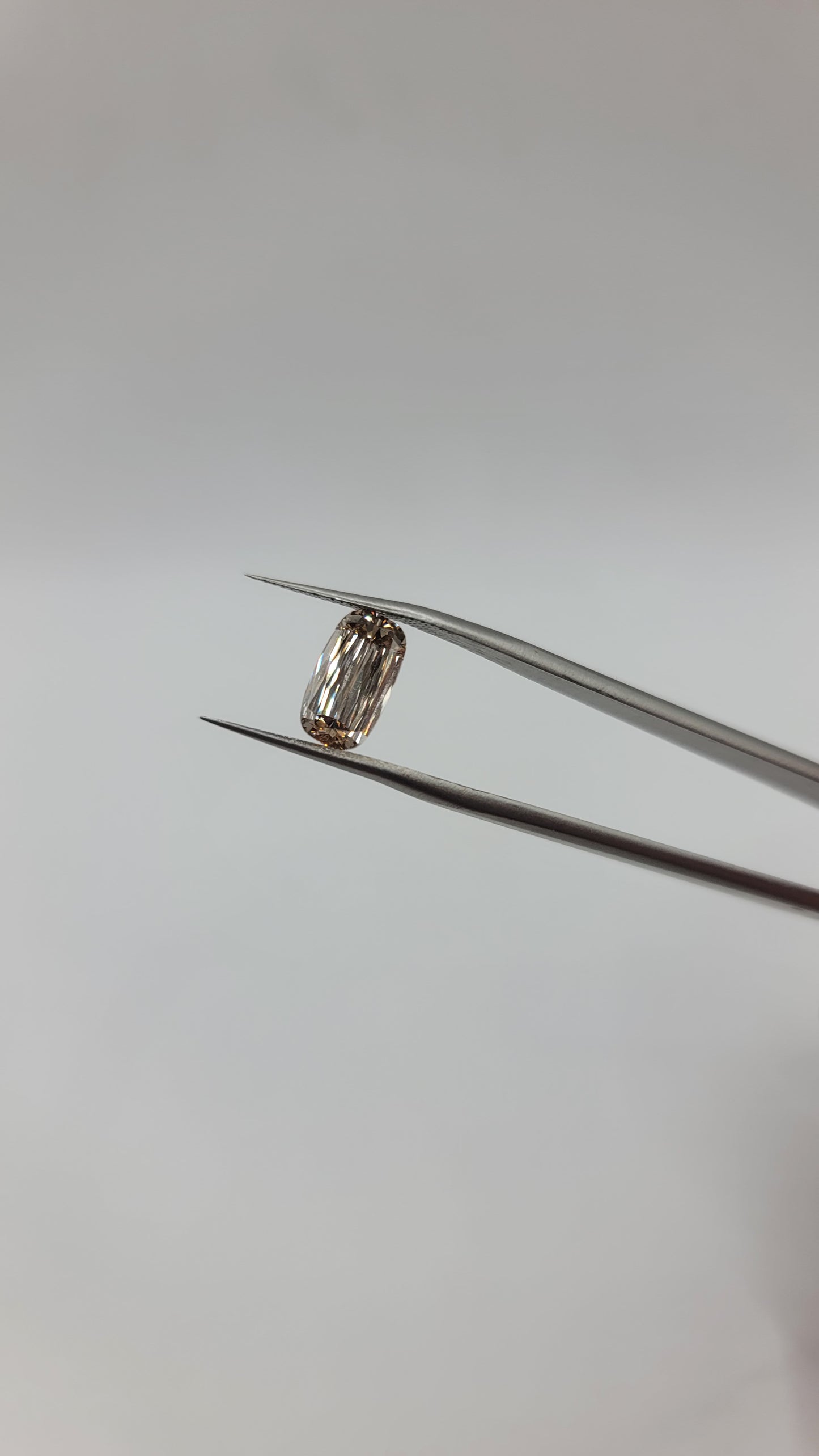 A lab grown crisscut diamond held between metal tweezers against a plain light gray background.