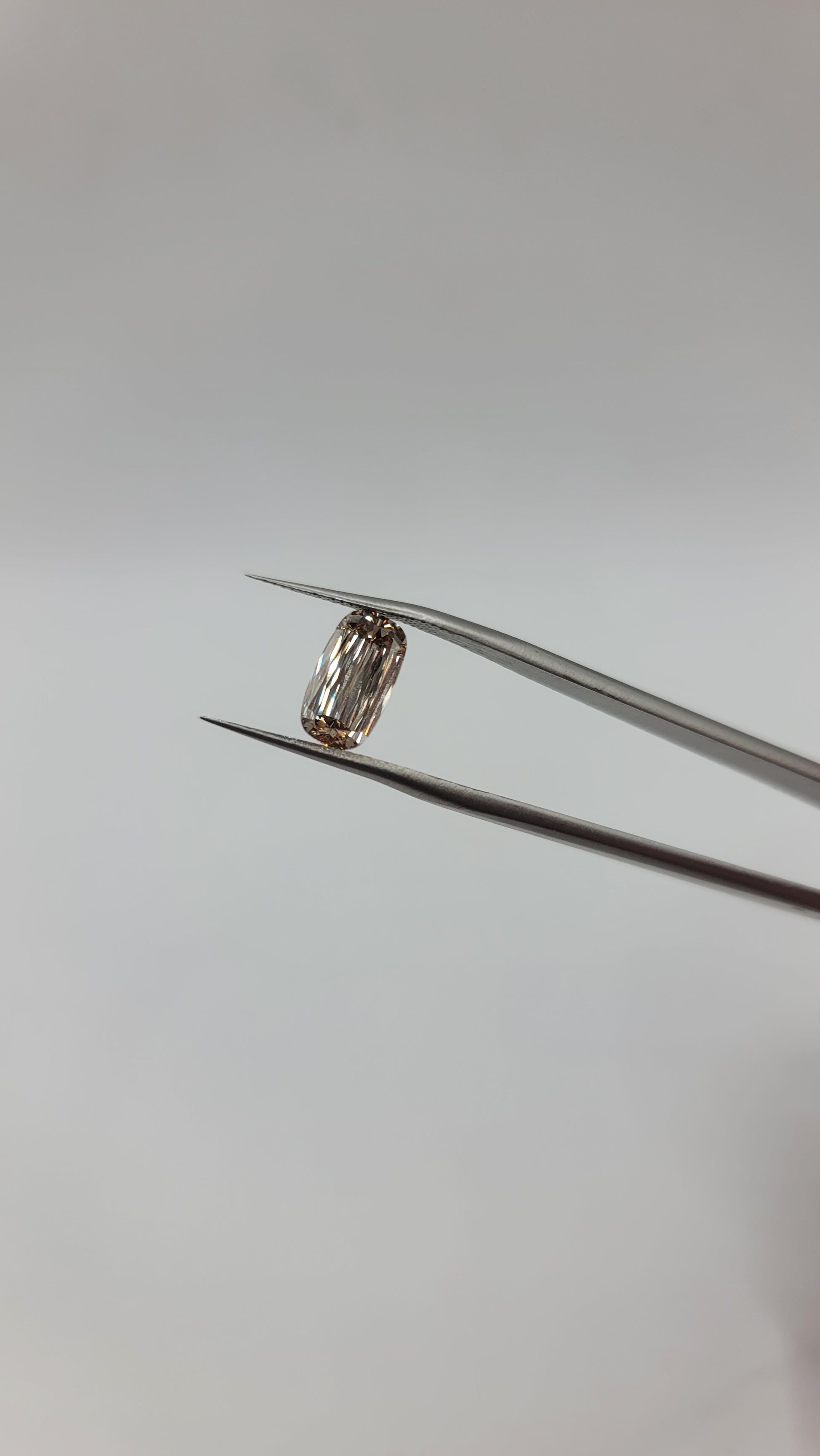 A lab grown crisscut diamond held between metal tweezers against a plain light gray background.