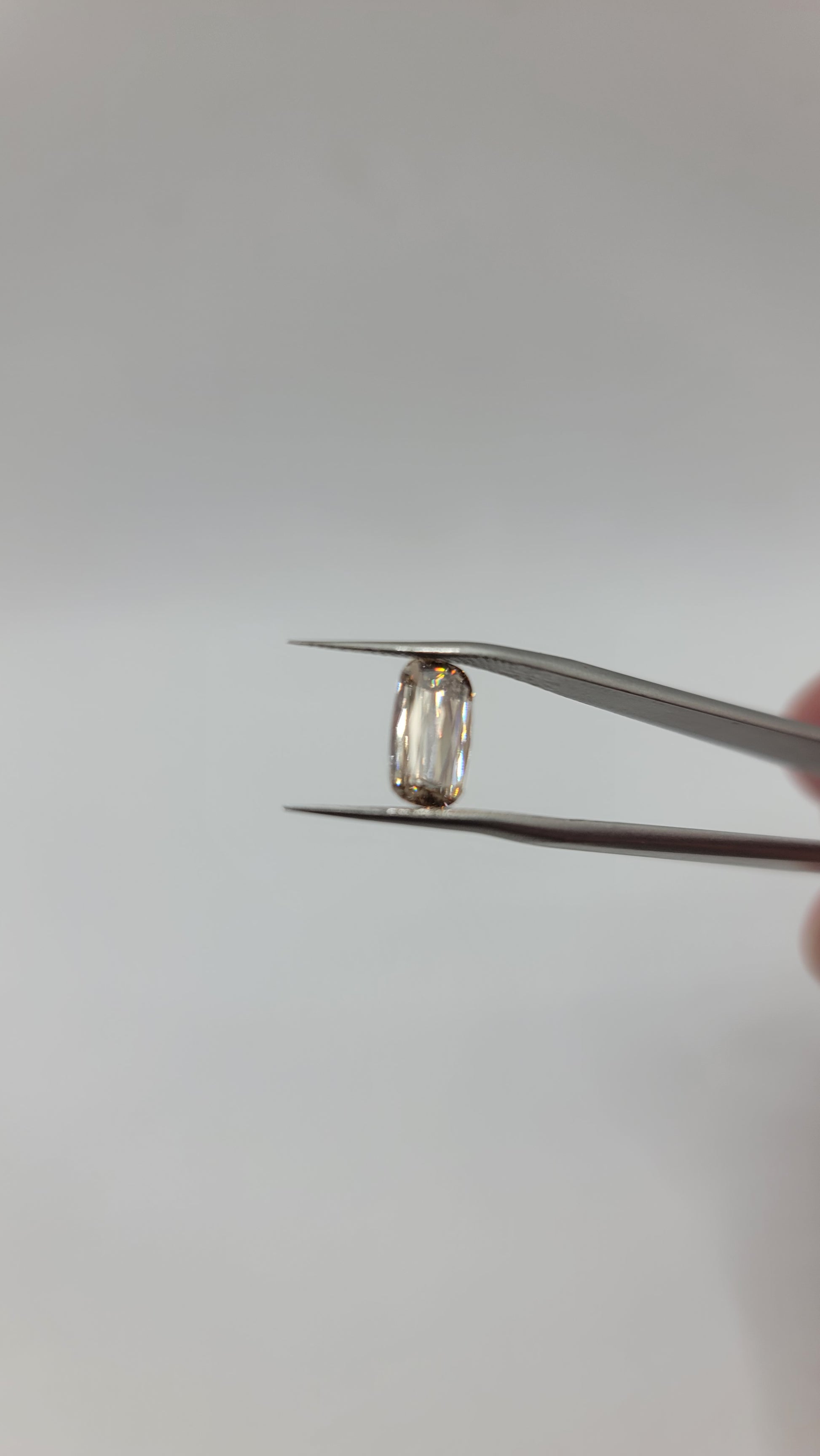 A lab grown crisscut diamond held between metal tweezers against a plain light gray background.