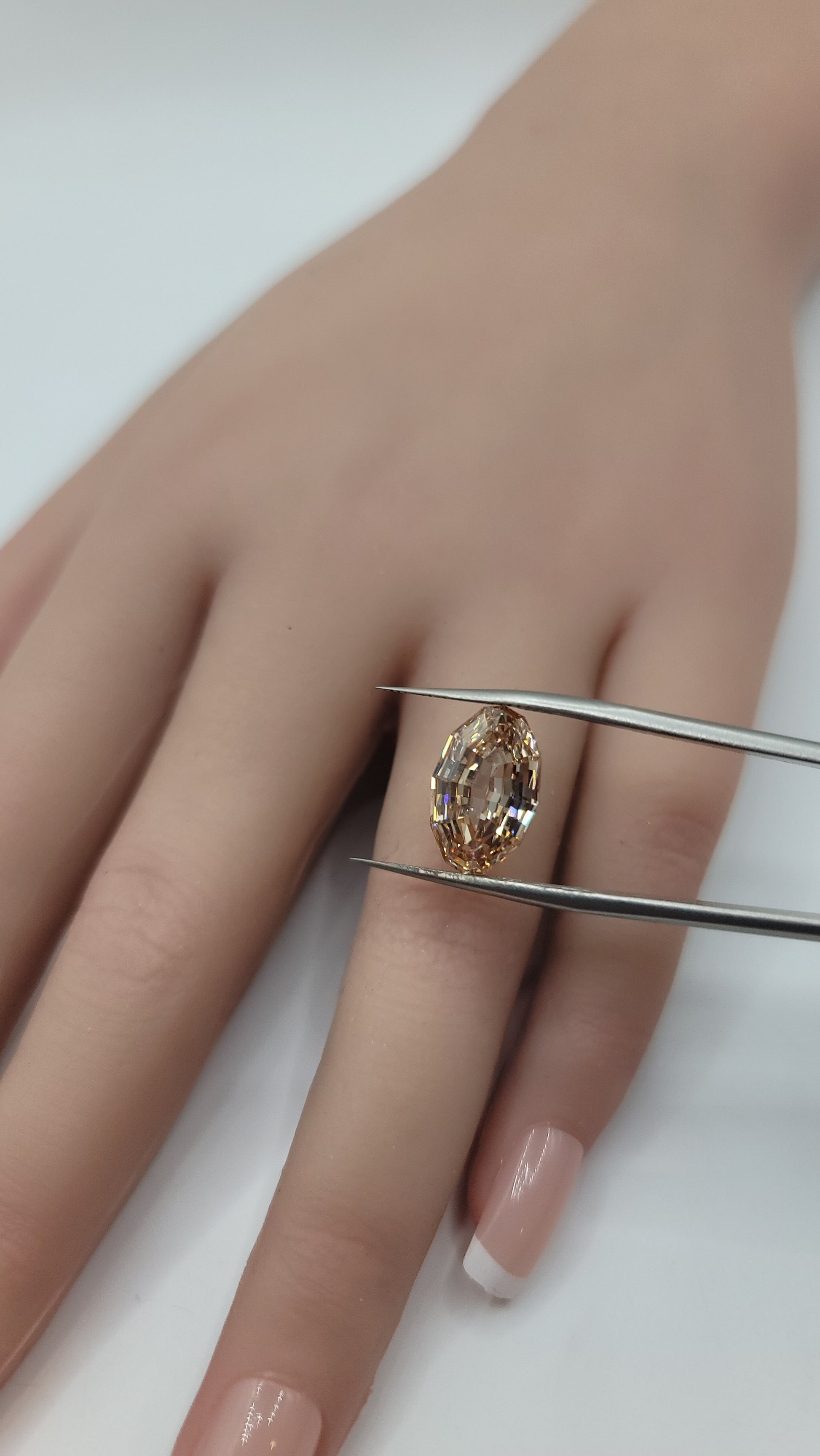 A close-up of a hand holding tweezers that are holding a oval lab diamond..
