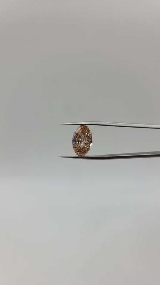 A oval lab diamond between two metal tweezers against a plain light gray background.