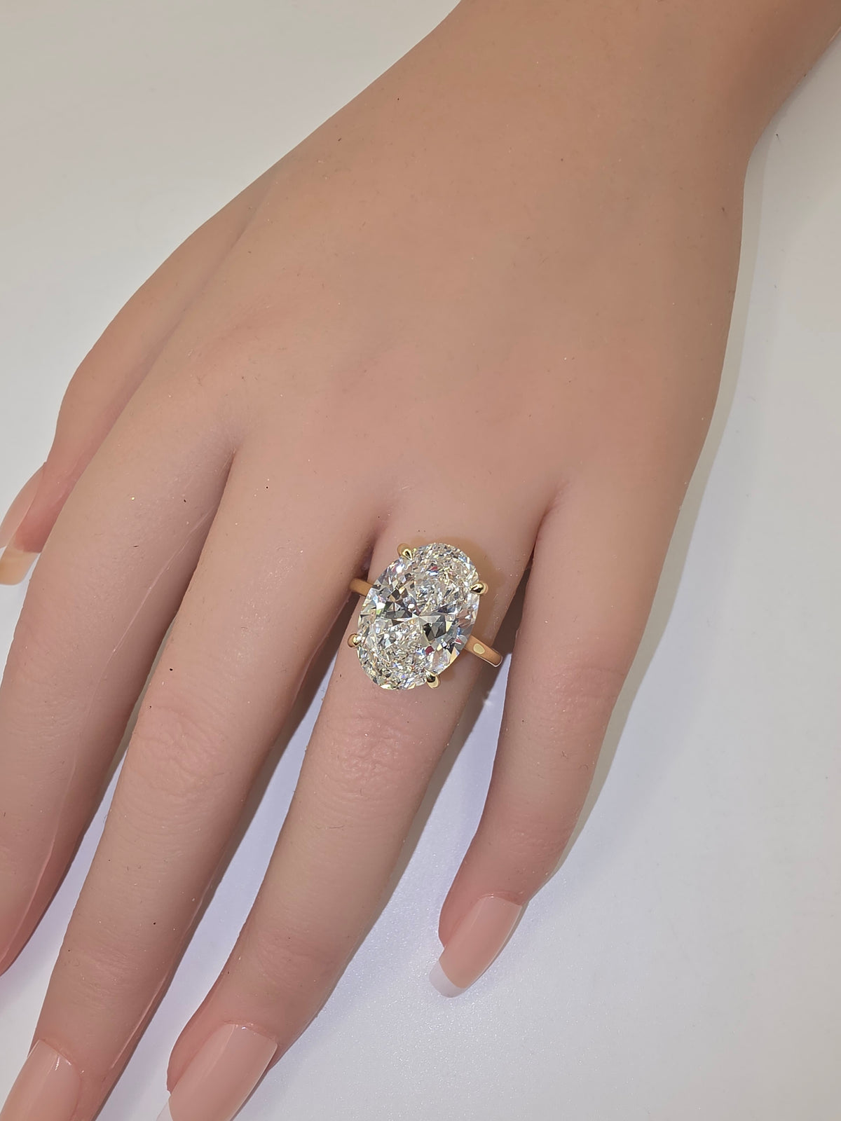 A close-up of a hand wearing a yellow gold ring with a large oval-cut clear gemstone, set against a plain light background.