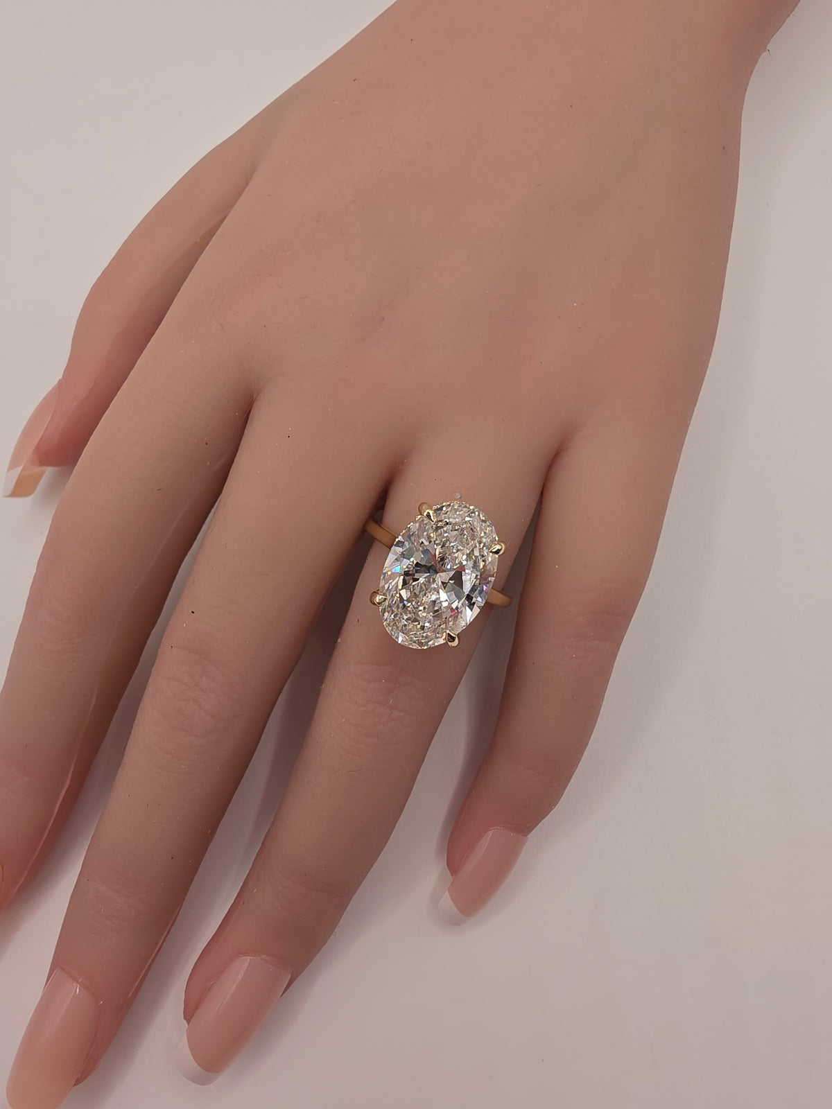 A close-up of a hand wearing a yellow gold ring with a large oval-cut clear gemstone in a prong setting, shown against a plain light background.