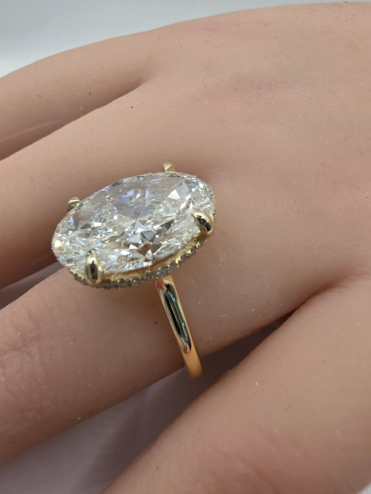 A yellow gold ring with a large oval-cut clear gemstone in a prong setting, shown worn on a person's finger.