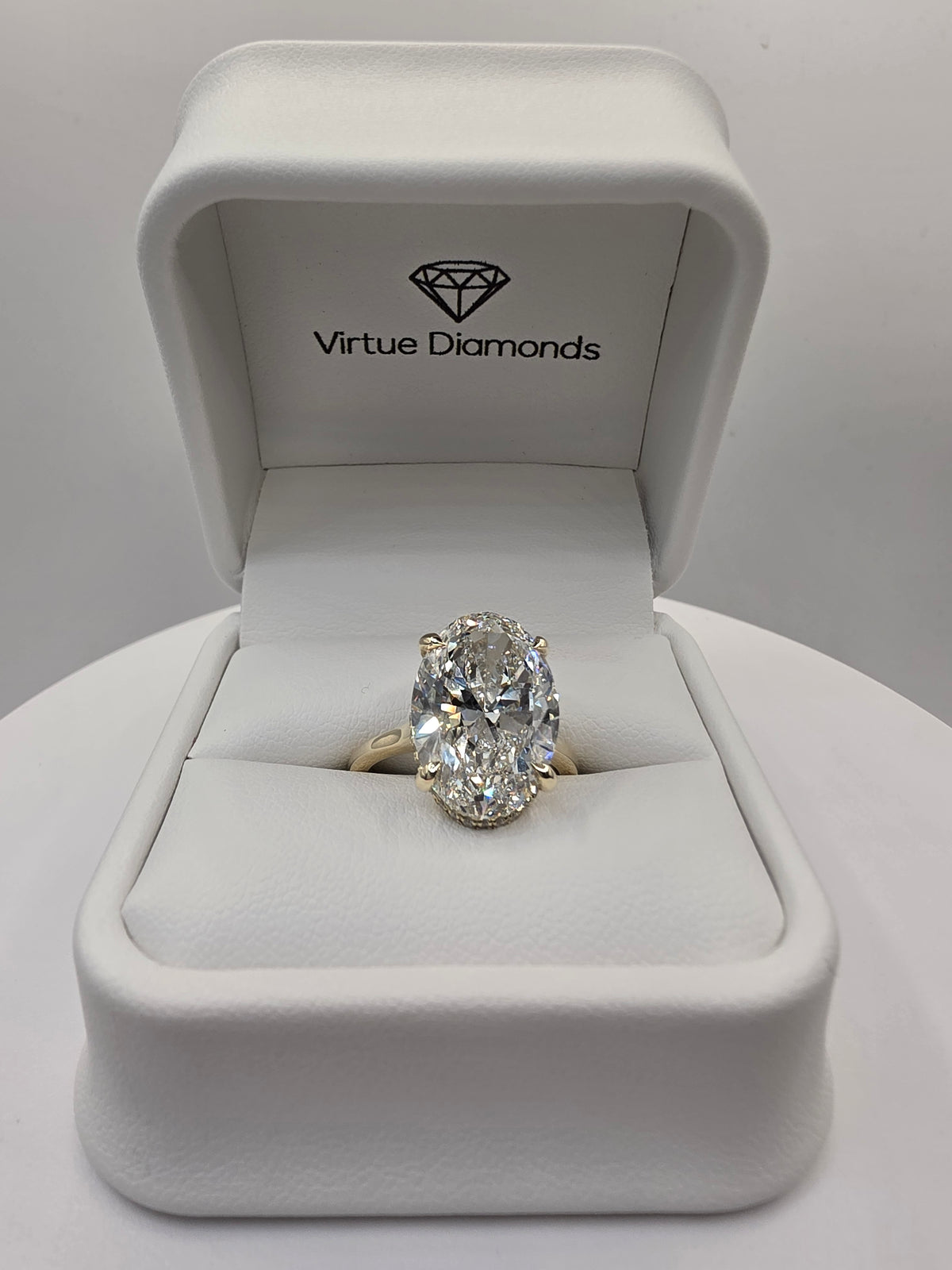 An oval-cut diamond ring with a yellow gold band, displayed inside an open white Virtue Diamonds presentation box.