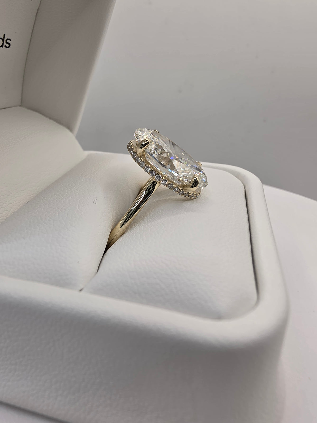 A yellow gold ring with a large oval clear gemstone and small accent stones, displayed in a white ring box.