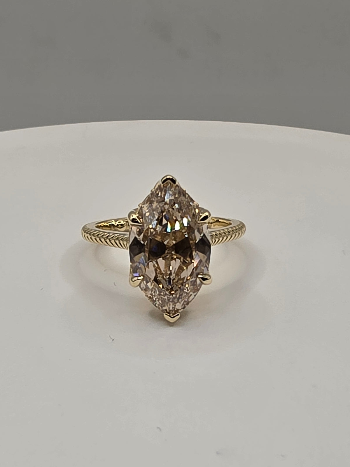 A gold ring featuring a large marquise-cut brown gemstone in a four-prong setting, displayed on a white surface against a gray background.