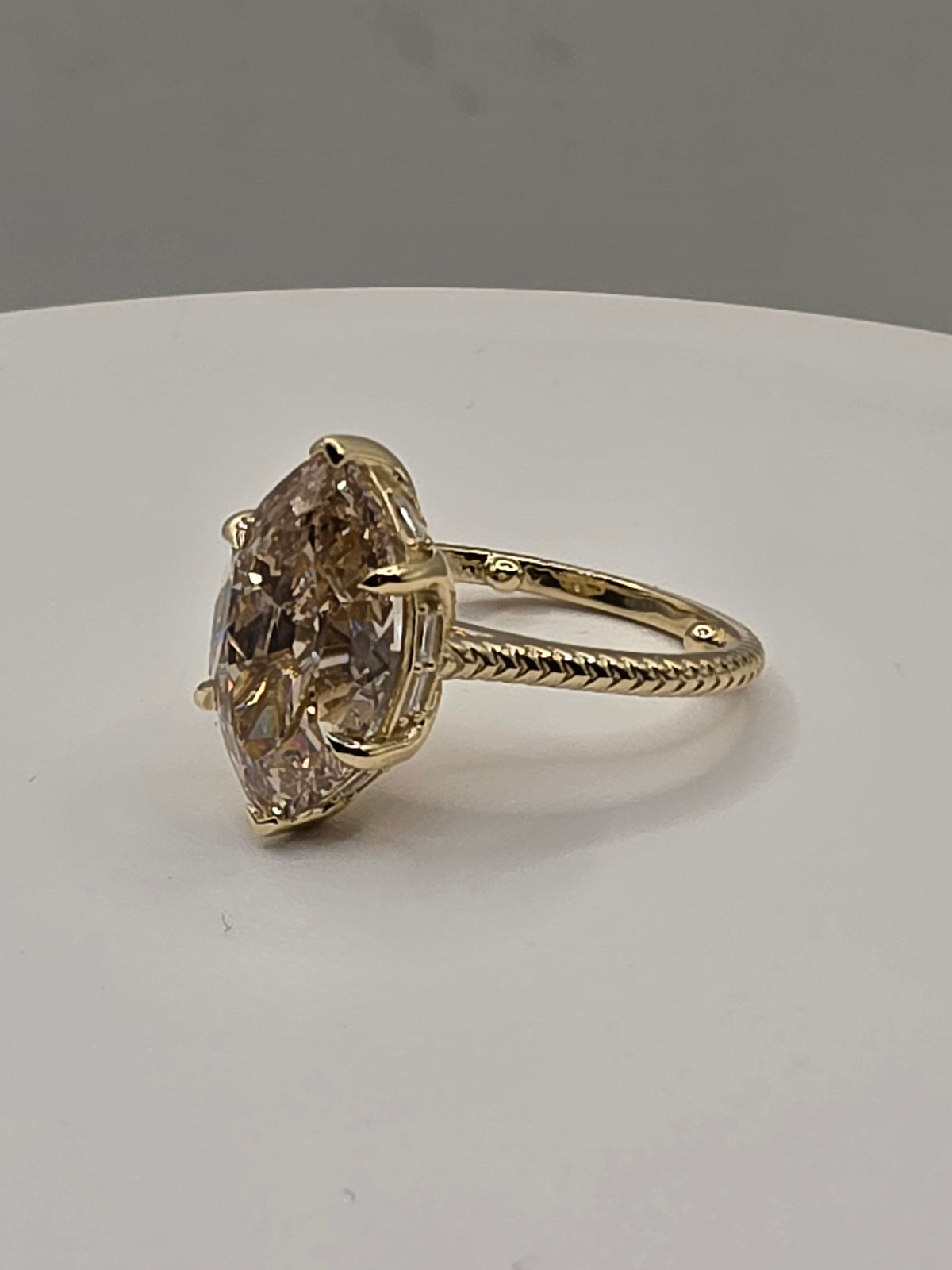 A yellow gold ring featuring a large marquise-cut champagne-colored diamond, displayed on a white surface against a neutral gray background.