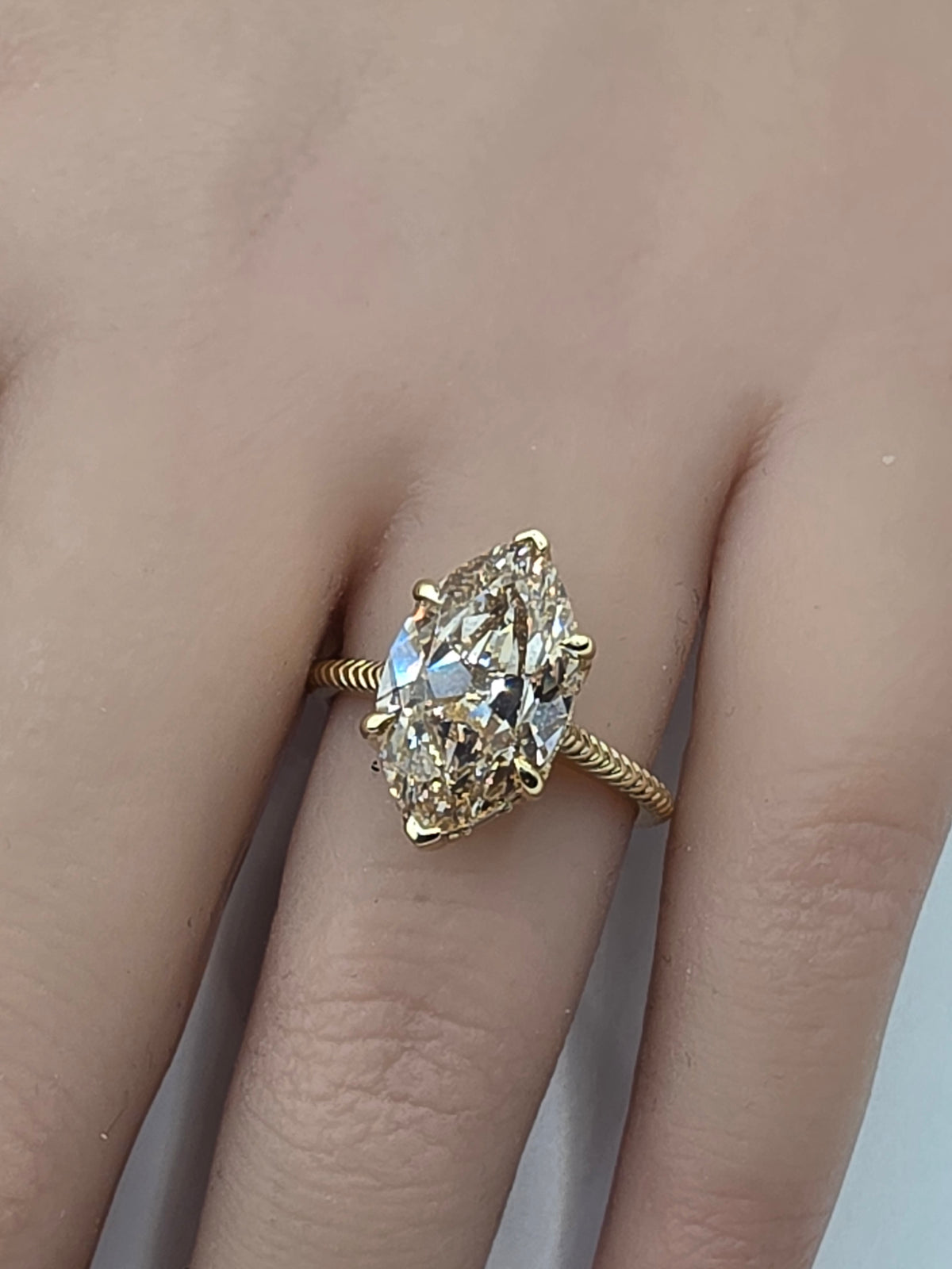 A close-up of a hand wearing a yellow gold ring with a large marquise-cut clear gemstone.