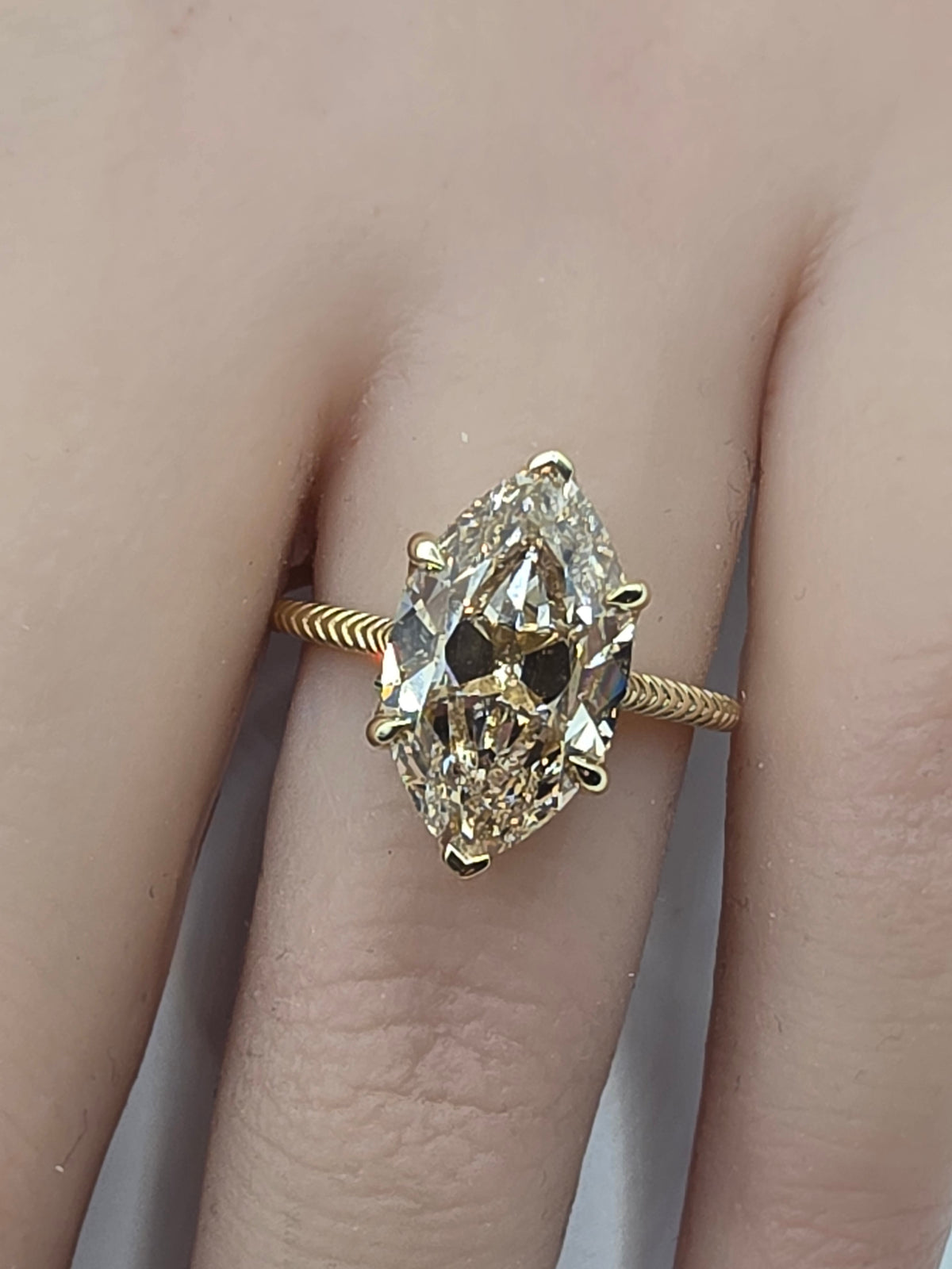 A close-up of a gold ring with a large marquise-cut diamond set on a finger. Per the instructions, clear gemstones do not contribute to the color, so the product color is determined solely by the gold metal setting.