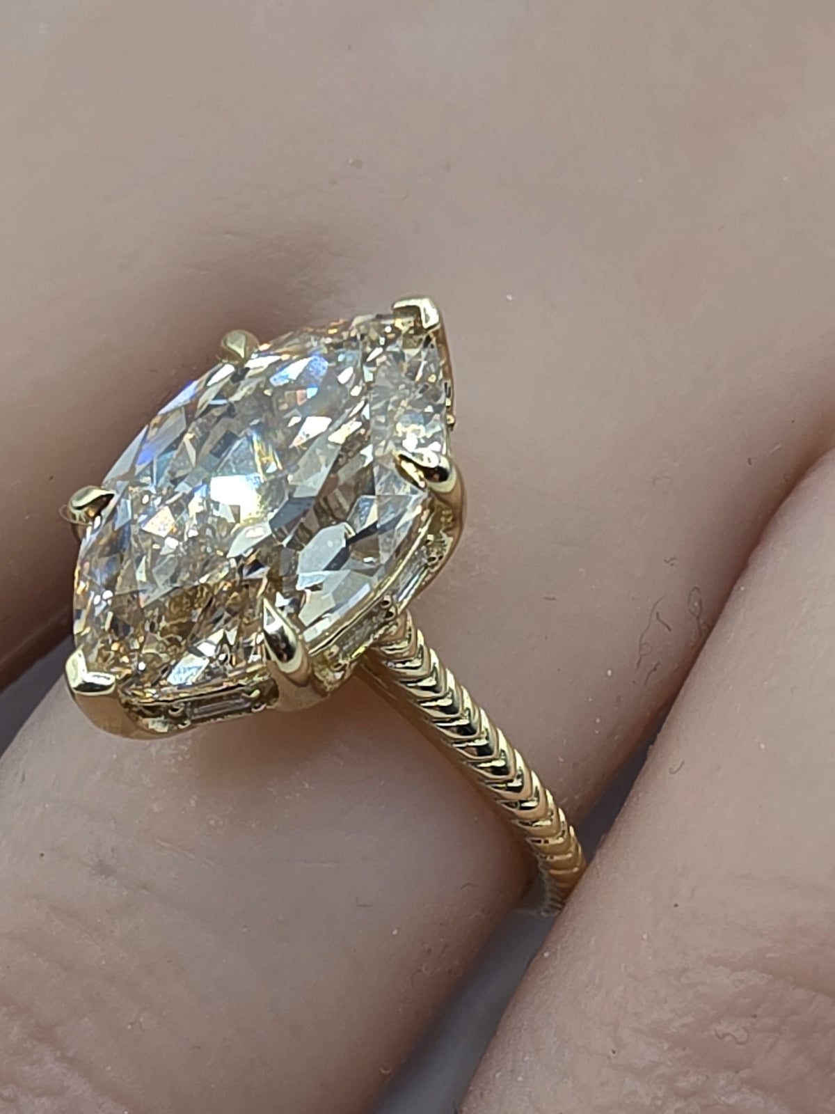 A yellow gold ring with a large marquise-cut clear gemstone, worn on a finger. The ring features a textured twisted band and is set in a four-prong setting.