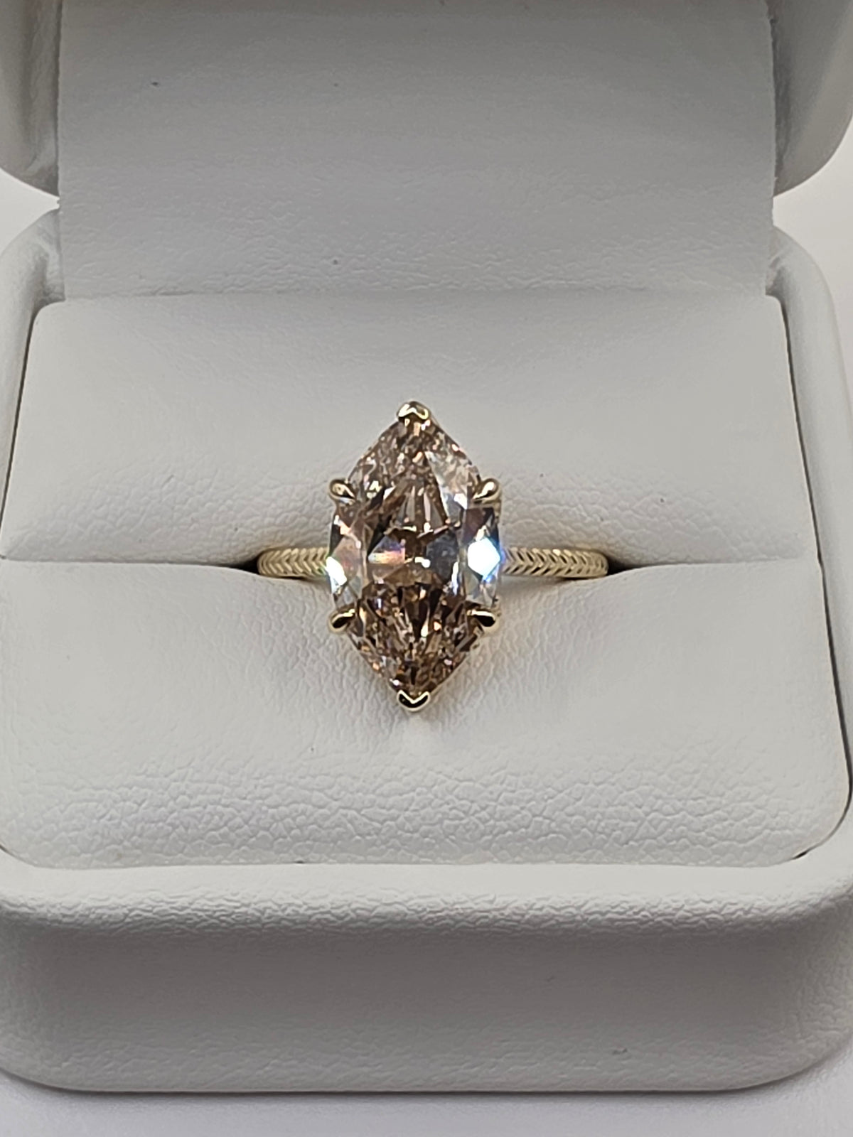 A yellow gold ring with a marquise-cut clear gemstone, displayed inside an open white ring box.