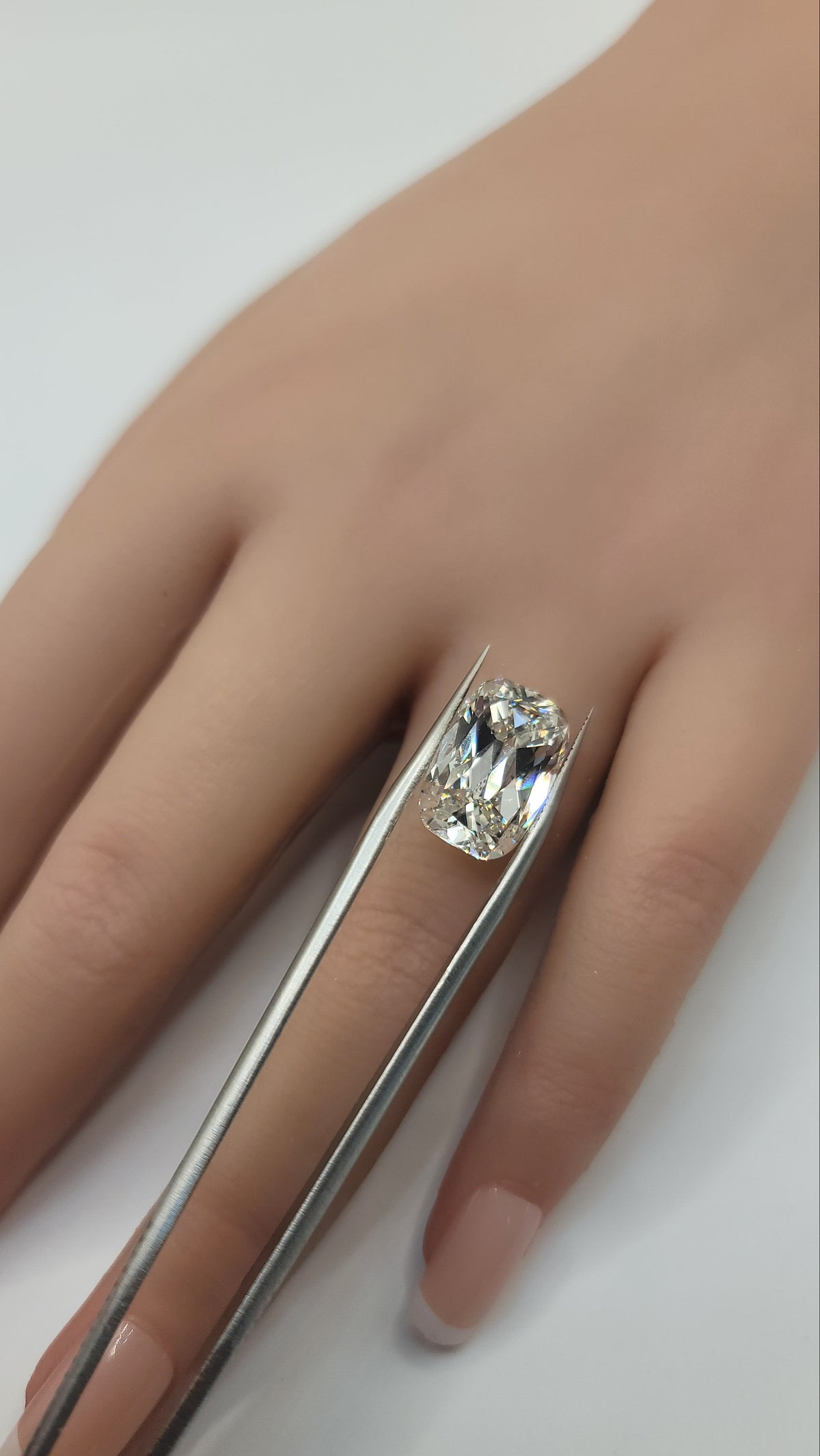 A close-up of a hand holding a silver ring with a rectangular clear gemstone, using metal tweezers to position it, against a plain white background.