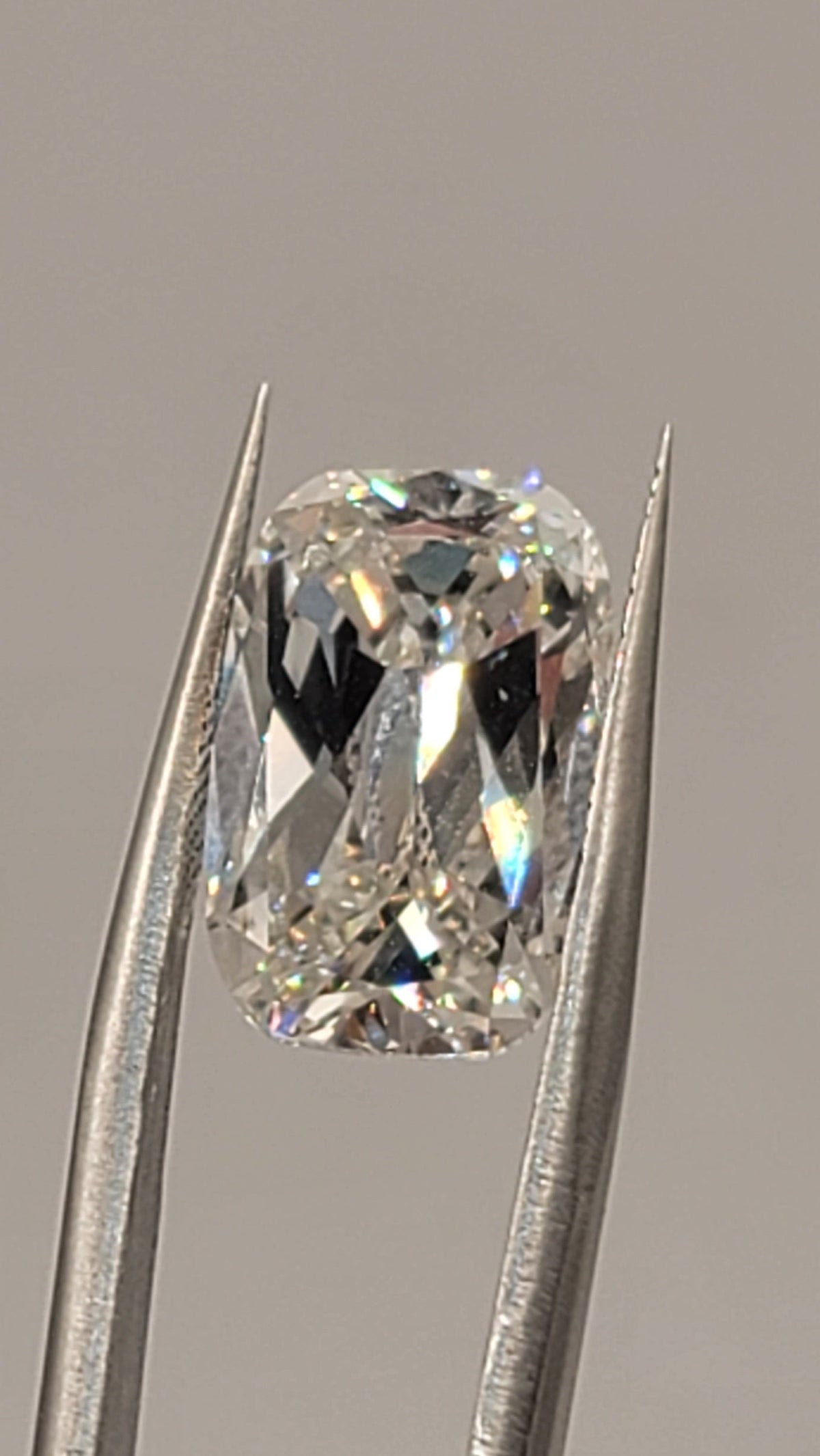 A loose cushion-cut diamond held between metal tweezers against a plain light gray background.