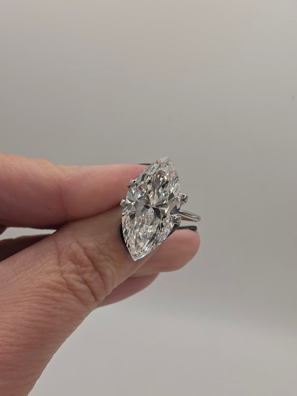 A hand holding a large marquise-cut diamond ring set in silver-toned metal against a plain light gray background.