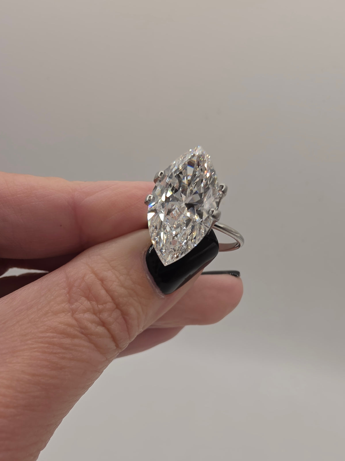 A hand holding a silver ring with a large marquise-cut clear gemstone, shown against a plain light gray background.