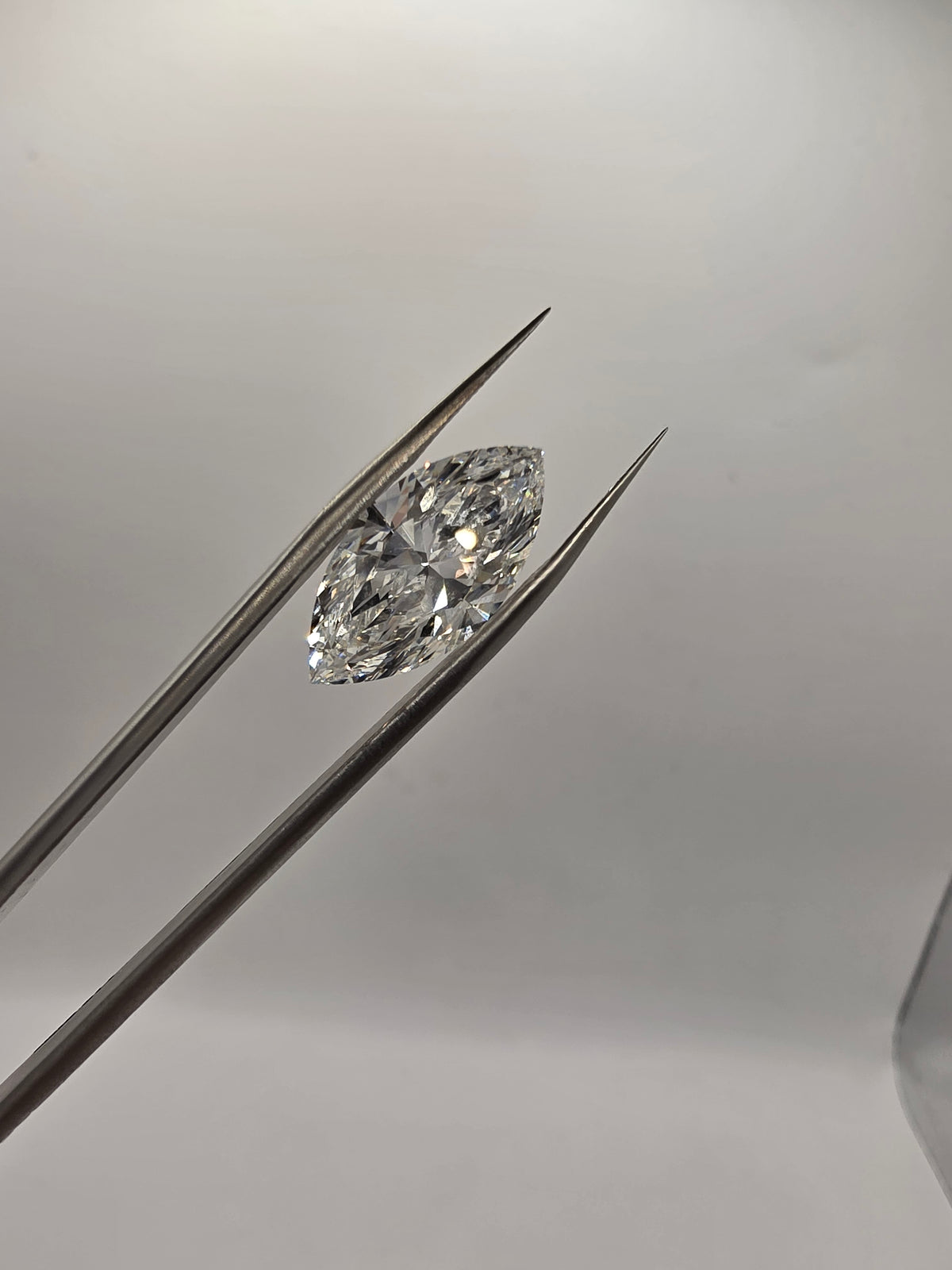 A marquise-cut clear gemstone held between metal tweezers against a soft light gray background.