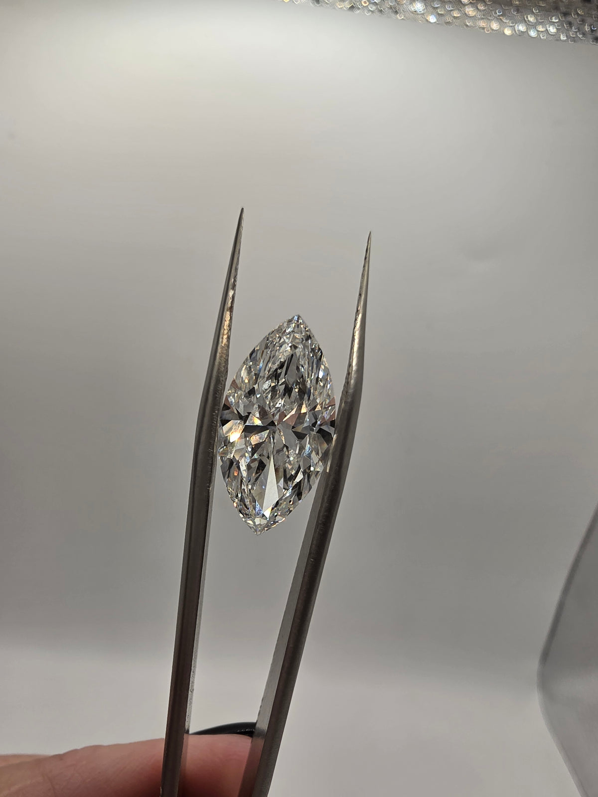 A marquise-cut diamond held in silver tweezers against a plain light gray background.