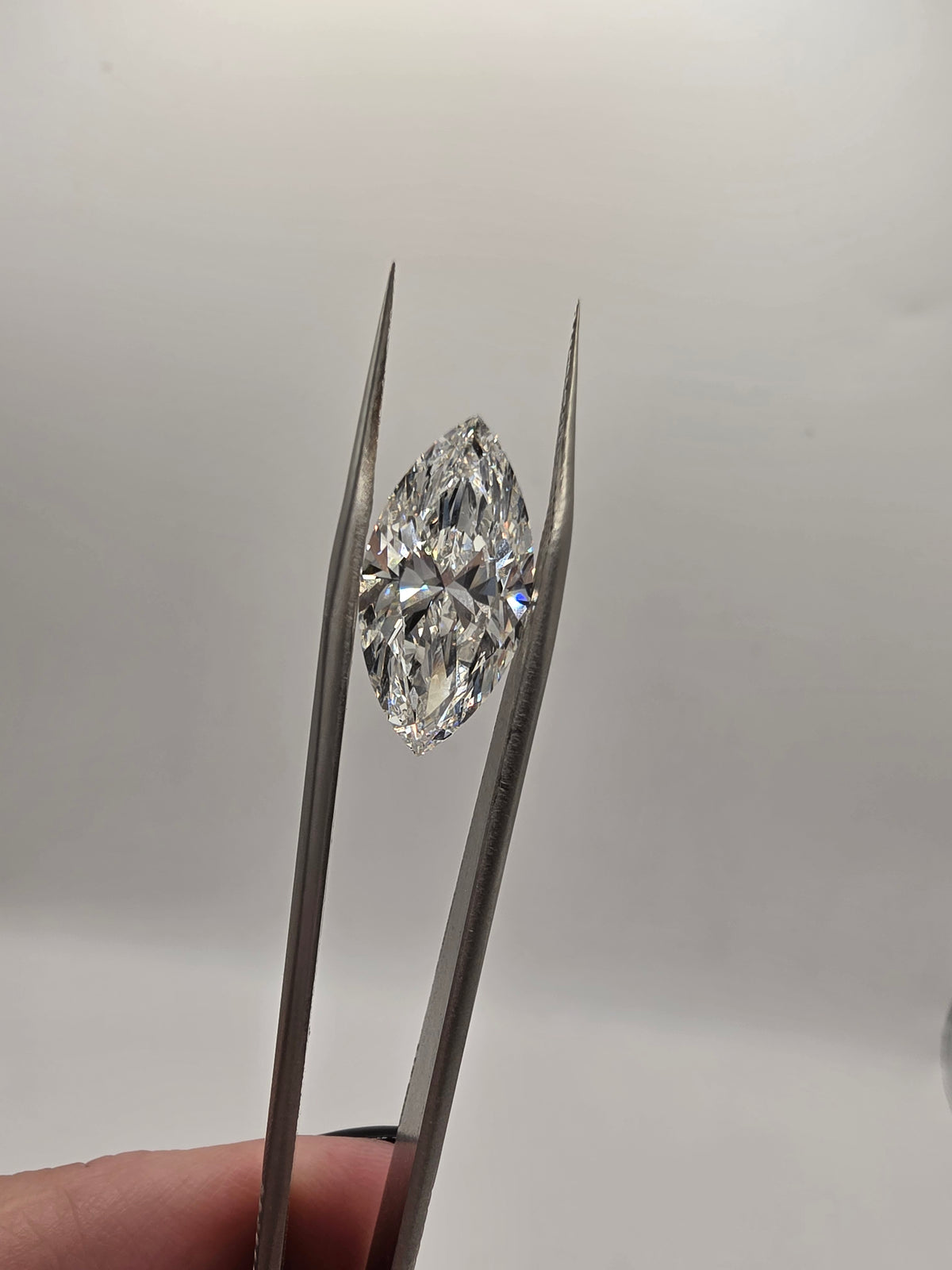 A marquise-cut diamond held between metal tweezers against a plain light gray background.