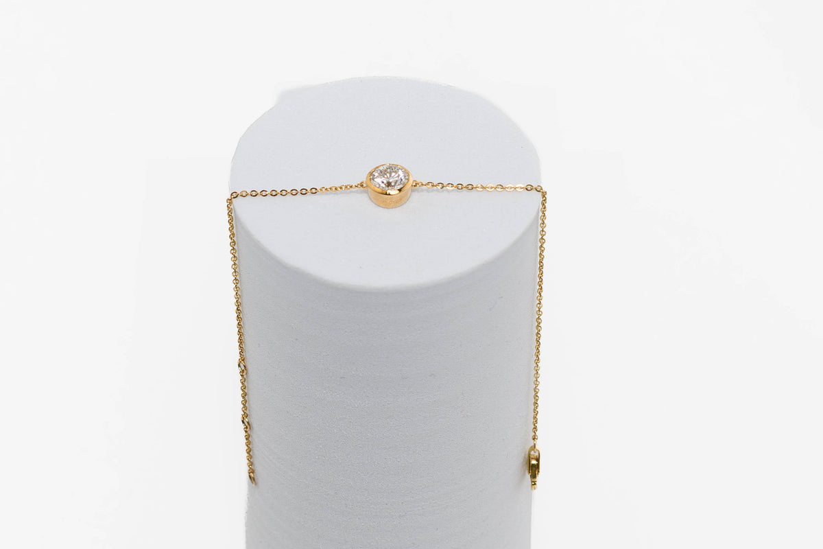 Solitaire bracelet in yellow gold on a white cyinder on plain background