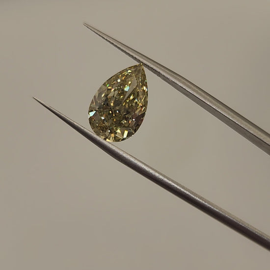 Yellow diamond being held by tweezers in front of grey background