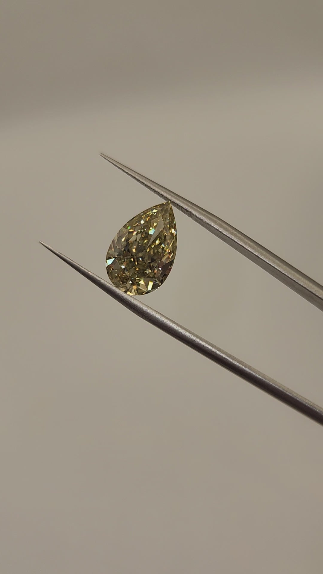 Yellow diamond being held by tweezers in front of grey background