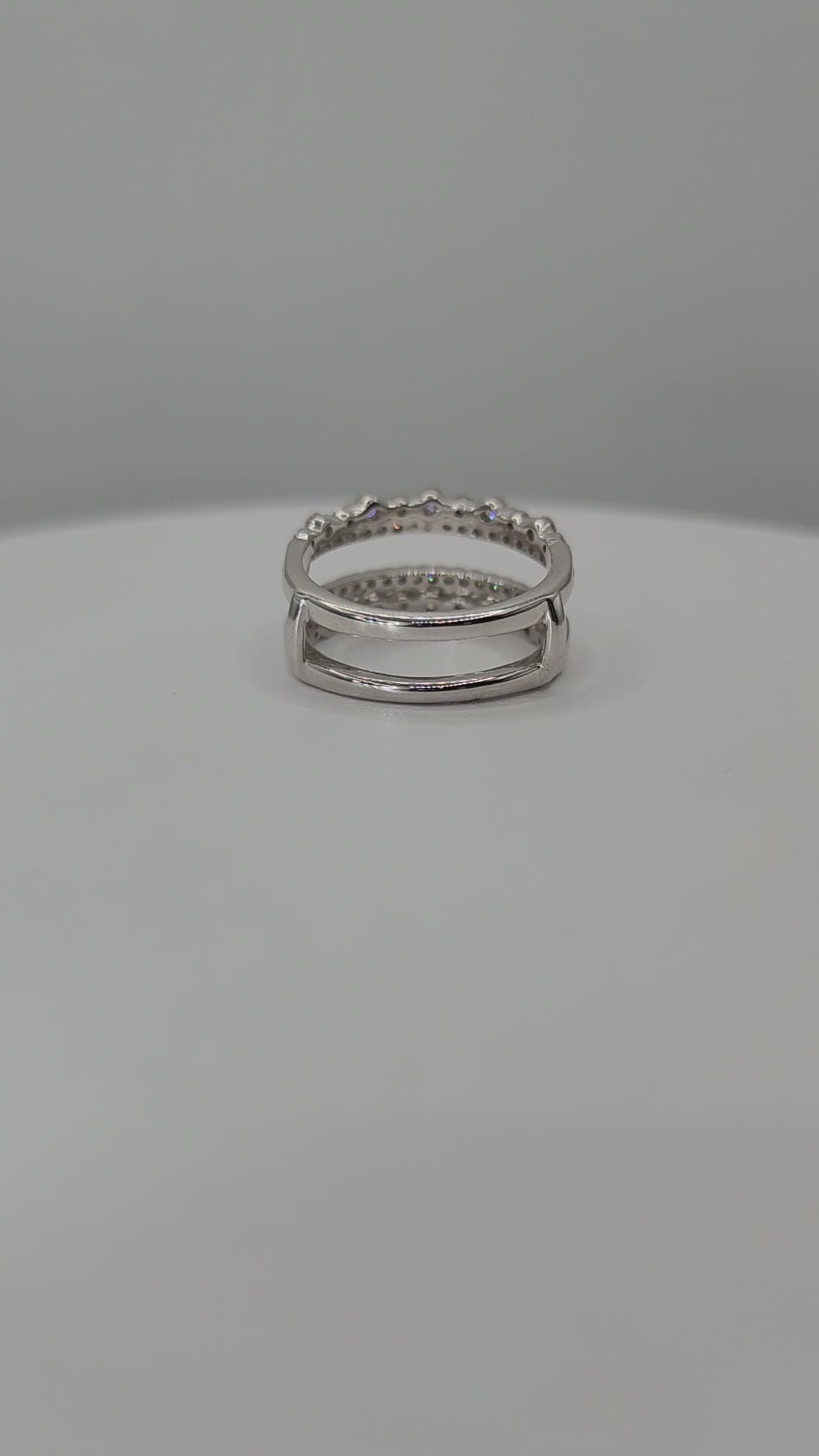 White Gold  ring with embedded stones on a white stand against a gray background