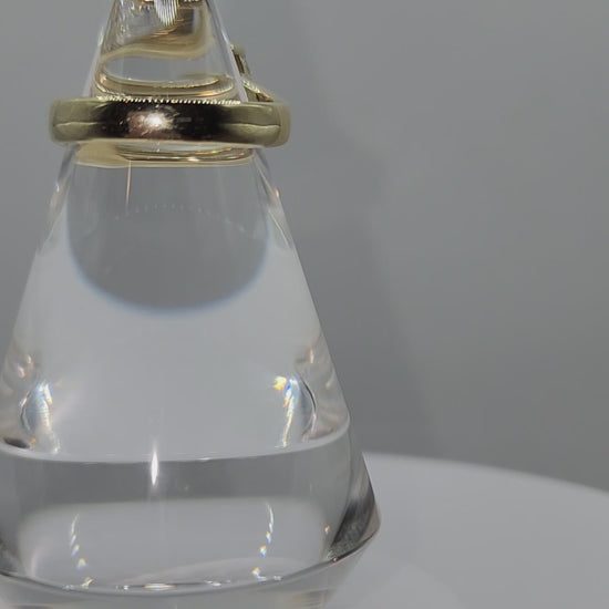 Diamond and yellow gold ring on a clear display spinning in front of a grey back ground