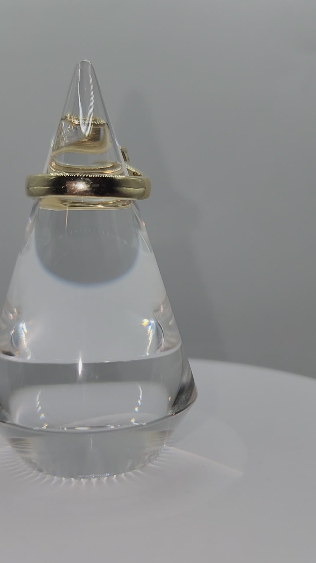 Diamond and yellow gold ring on a clear display spinning in front of a grey back ground