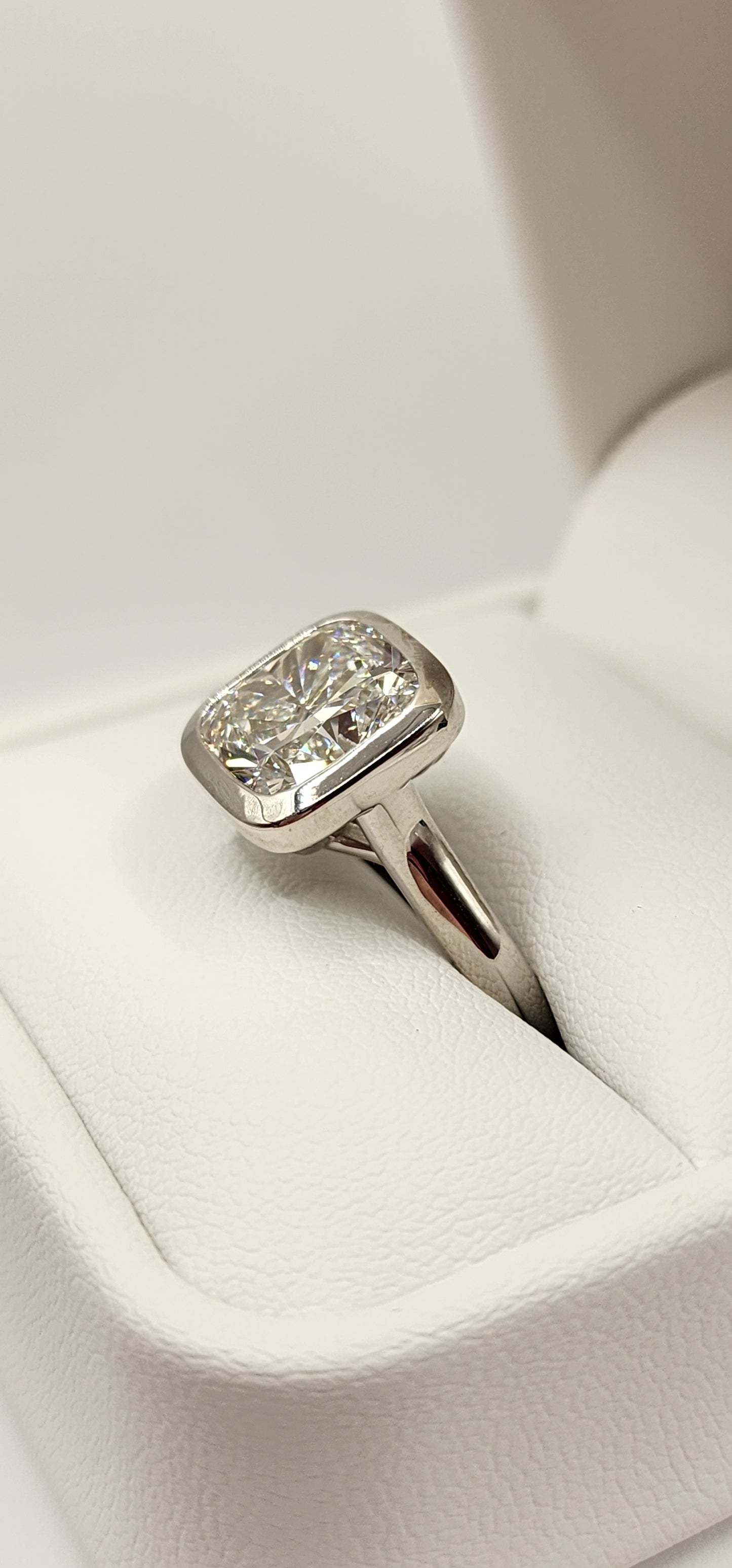 "The Brittney" is a 5.5 Carat Cushion Cut Lab Grown Diamond F/VS1, in a 14k White Gold Full Bezel, Cathedral Setting with Cross Cross Prongs